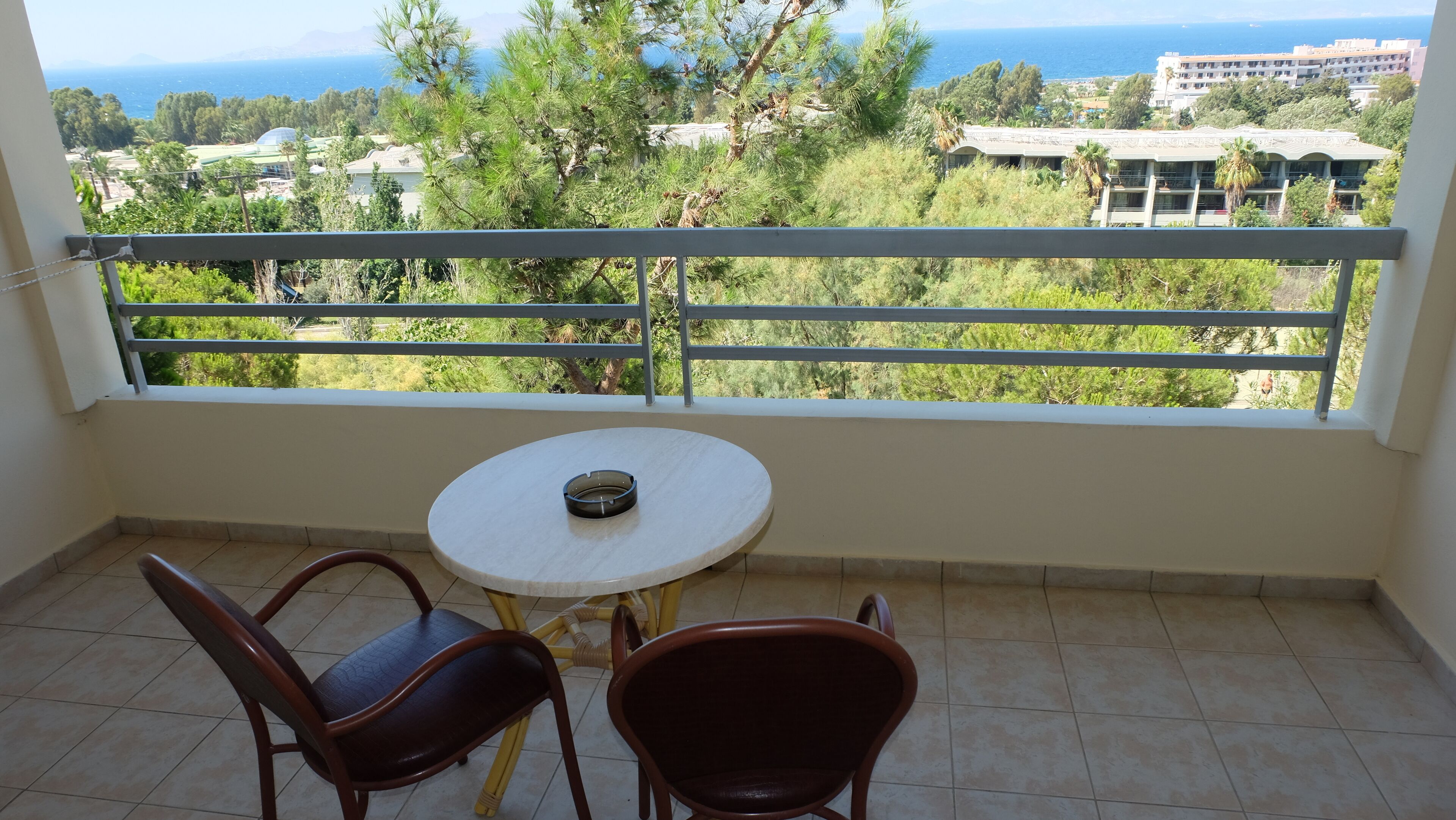 Un balcon avec une table et deux chaises, offrant une vue panoramique sur les arbres et les bâtiments.