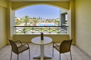 Un balcon donnant sur une piscine, deux fauteuils en osier et une table ronde.