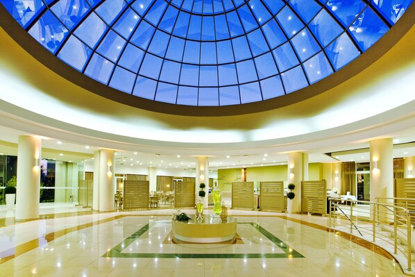 Un hall d’entrée spacieux avec une table ronde centrale, un plafond en verre et un comptoir d’accueil.