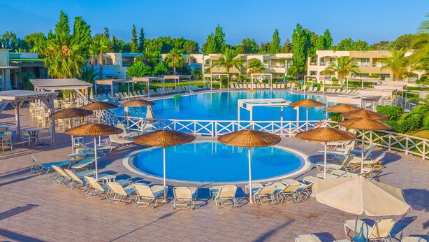 Une grande piscine extérieure entourée de chaises longues et de parasols, avec un espace aménagé au bord de la piscine et une vue sur les bâtiments de l’hôtel en arrière-plan.