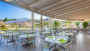 Un espace extérieur aménagé en terrasse, avec des tables rondes et des chaises en osier, offrant une vue sur une piscine et des bâtiments en arrière-plan.