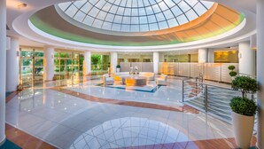 Un vaste atrium doté d’une verrière, un espace de détente central et un escalier menant aux étages supérieurs.