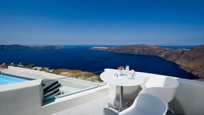 A terrace with a pool, white chairs, and a table set for two with a view of the sea and islands. - Avaton Resort and Spa (Santorini)