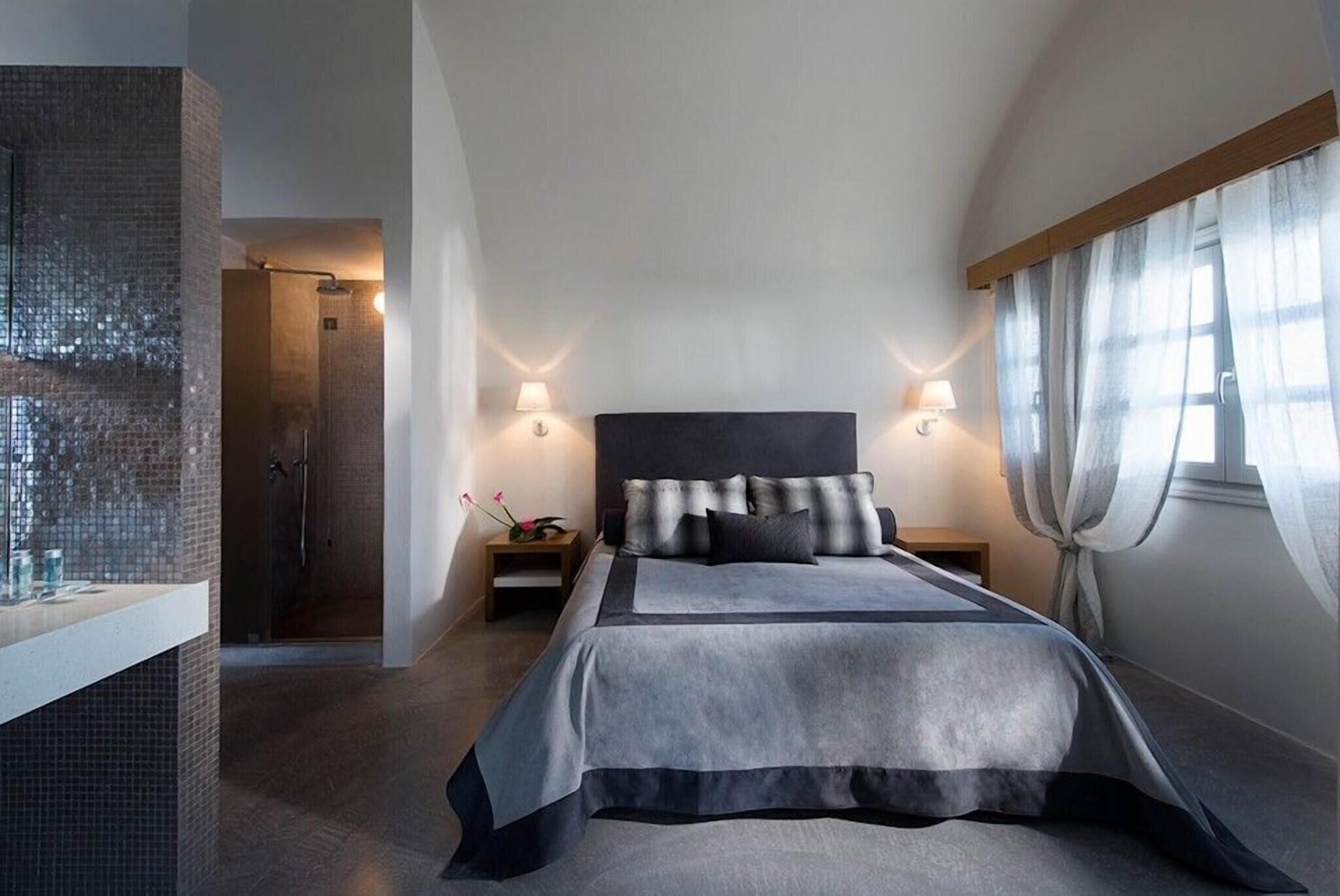 Un dormitorio moderno con una cama grande, lámparas de noche, zona de ducha y vistas al exterior.