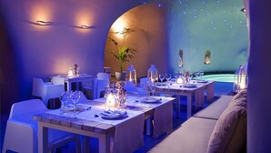 A restaurant with tables set for dining, ambient lighting, and a plant centerpiece. - Avaton Resort and Spa (Santorini)