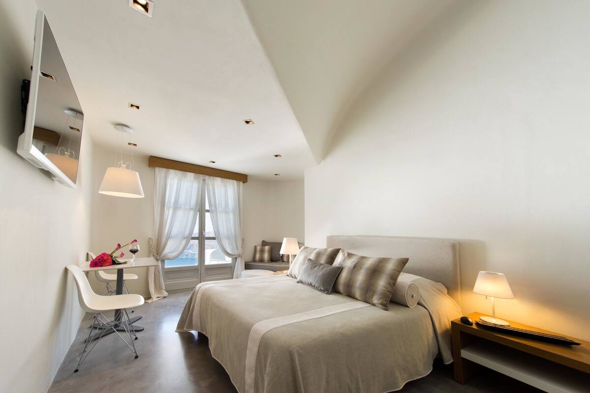 Un dormitorio moderno con una cama grande, mesitas de noche, un escritorio con silla y un ventanal con cortinas.
