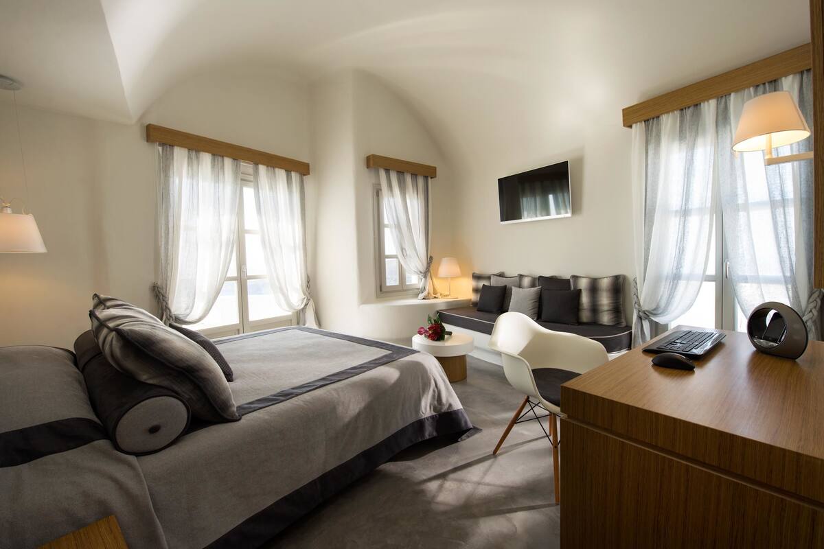 Una habitación de hotel moderna con una cama grande, un escritorio, una silla, un sofá y un televisor.