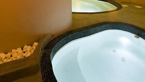 A spa area with a large hot tub, a smaller hot tub, and a seating area with pebbles. - Avaton Resort and Spa (Santorini)