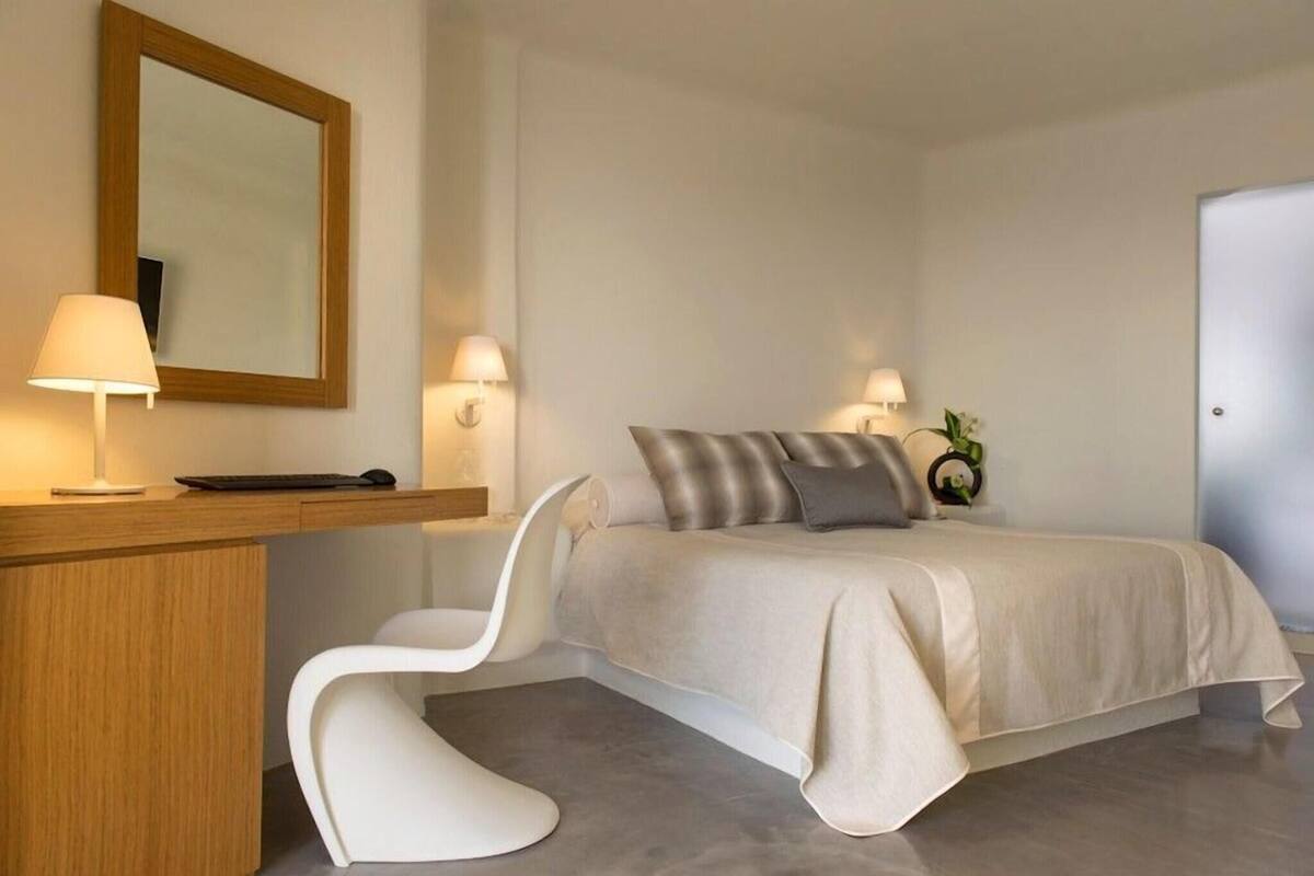 Un dormitorio con cama, lámparas de noche, un escritorio, una silla y un espejo.