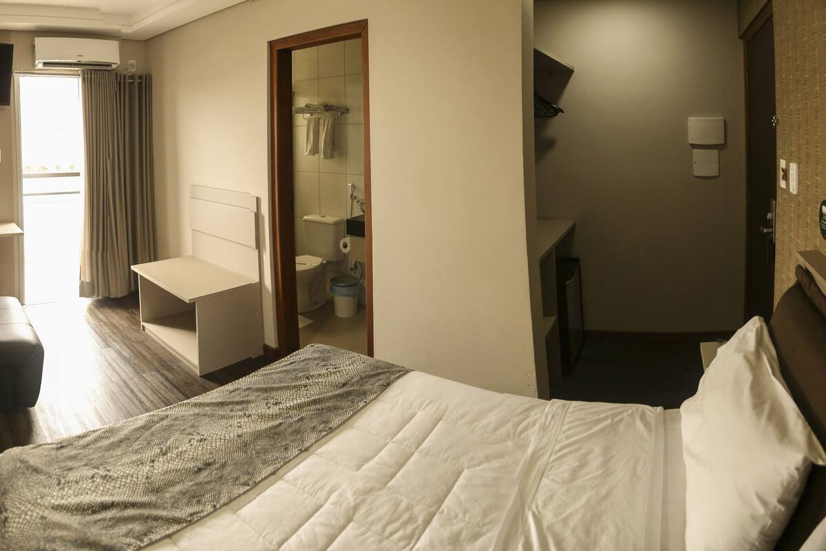 Una habitación de hotel con cama, escritorio, silla, televisor, baño y armario.