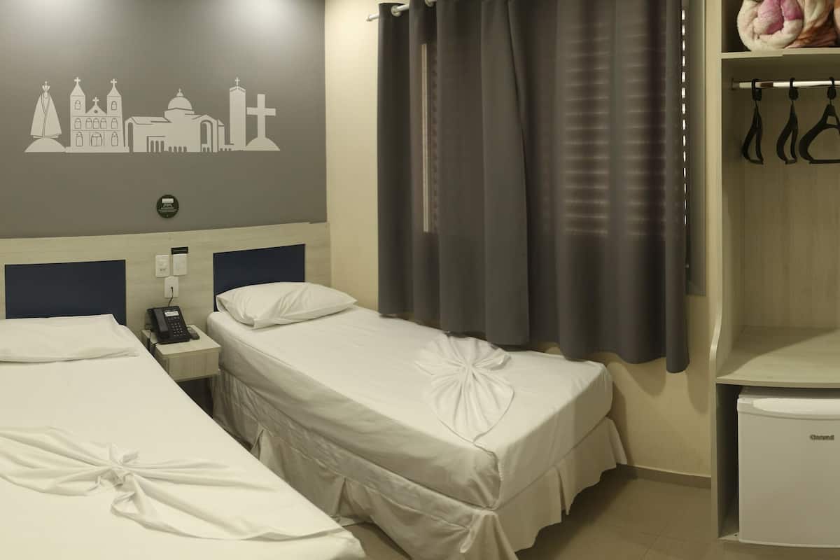 Habitación de hotel con dos camas individuales, un refrigerador pequeño, un armario con espacio para colgar ropa y una decoración religiosa en la pared.