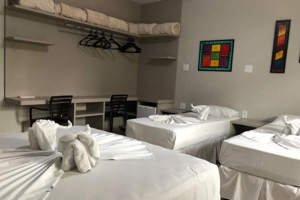 Habitación de hotel con dos camas, un escritorio, sillas y una pared con un cuadro colorido.