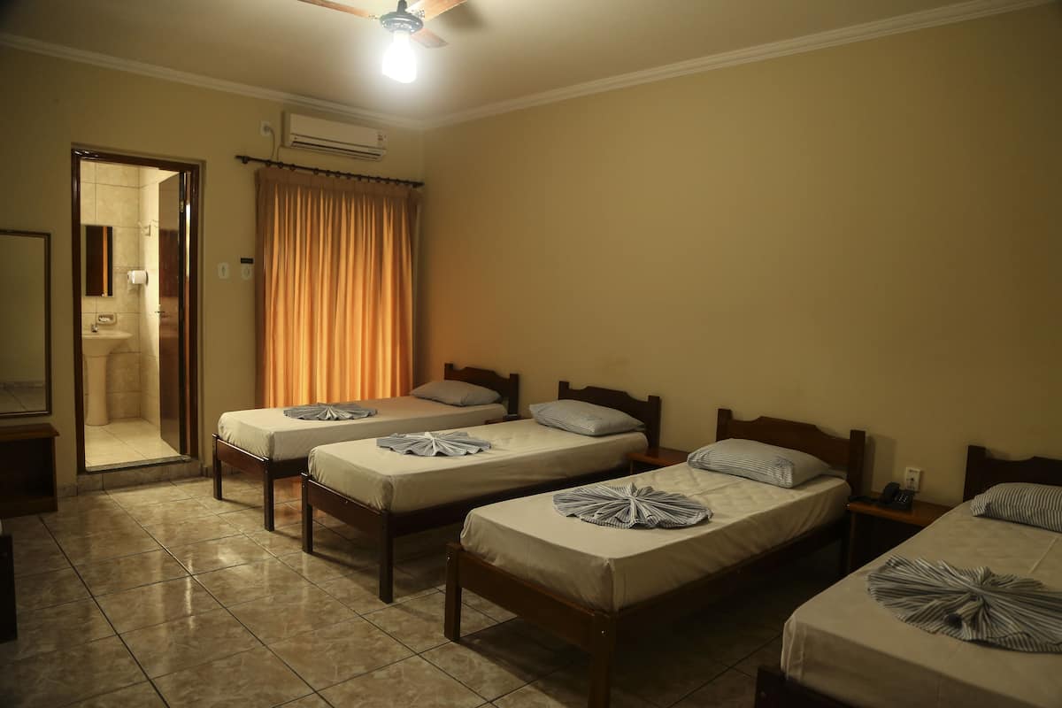Habitación de hotel con cuatro camas individuales, un baño con ducha y un ventilador de techo.
