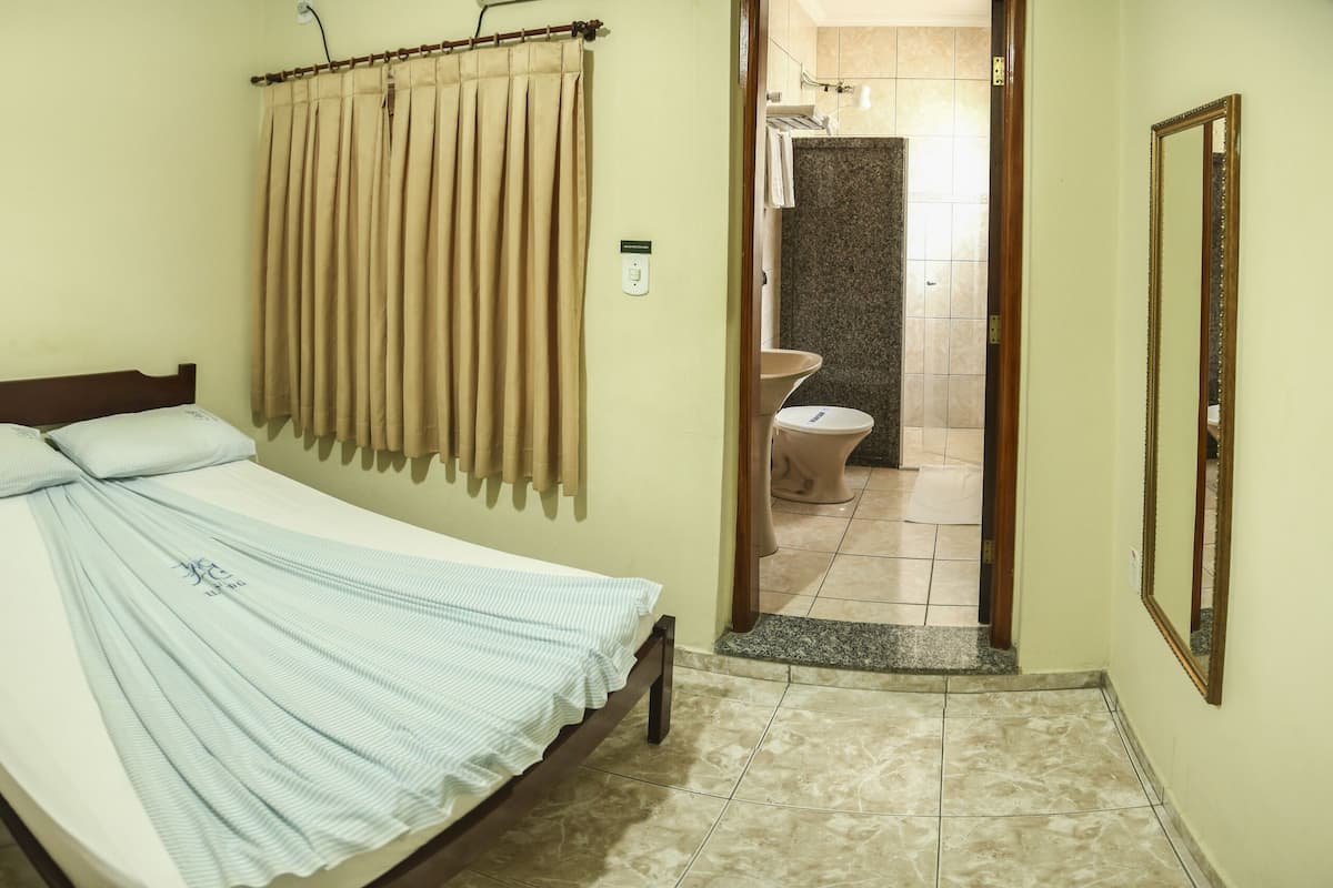 Un dormitorio con cama, mesita de noche, armario de madera, baño con inodoro y lavamanos, y zona de ducha.