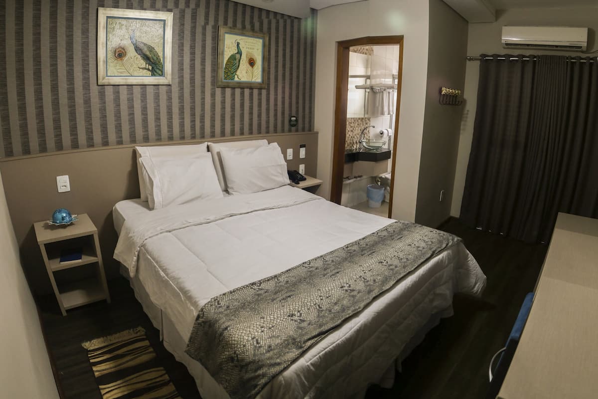 Una cama bien hecha con un edredón estampado, una mesita de noche con un objeto azul y dos cuadros en la pared.