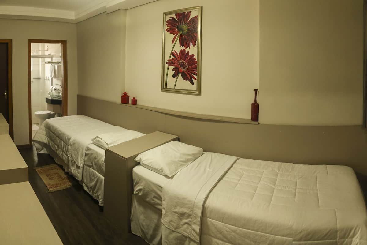 Habitación de hotel con dos camas individuales, un baño visible a través de una puerta abierta y una obra de arte floral grande en la pared.
