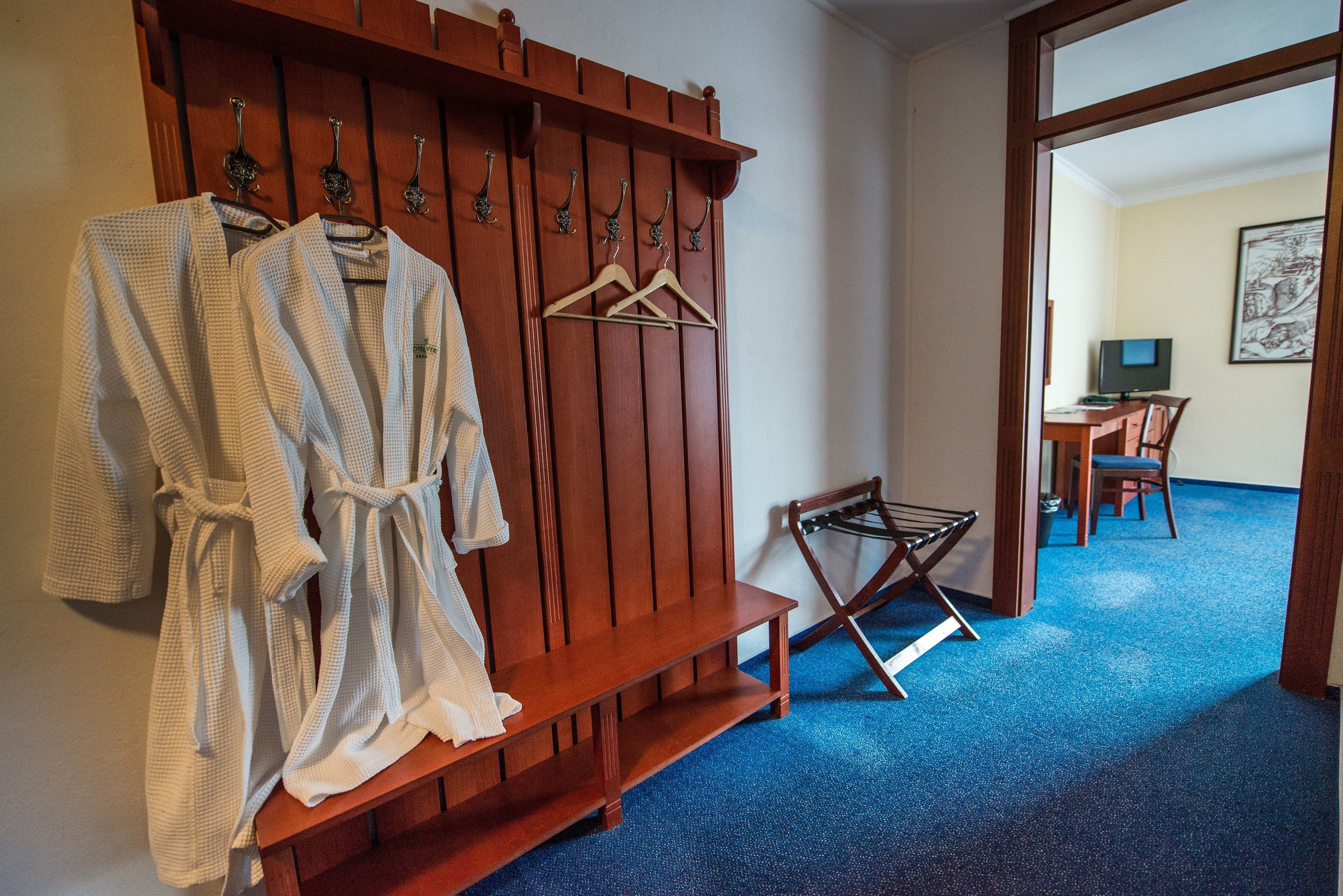 A hotel room with a wooden bench, a drying rack, and a desk with a chair.