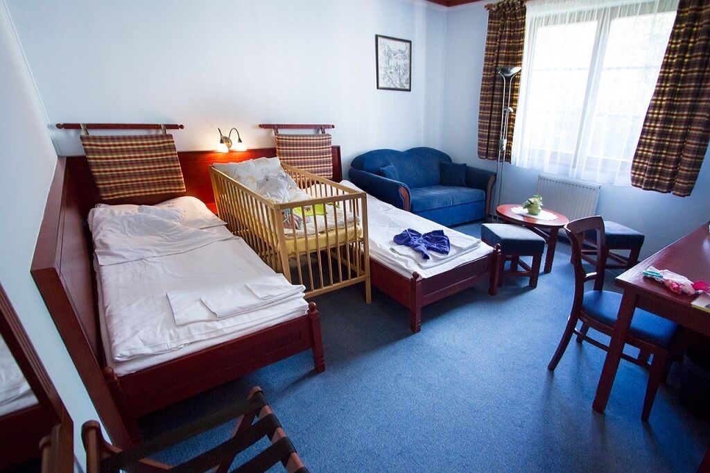 A room with a bed, a crib, a blue sofa, a small table, and a chair.