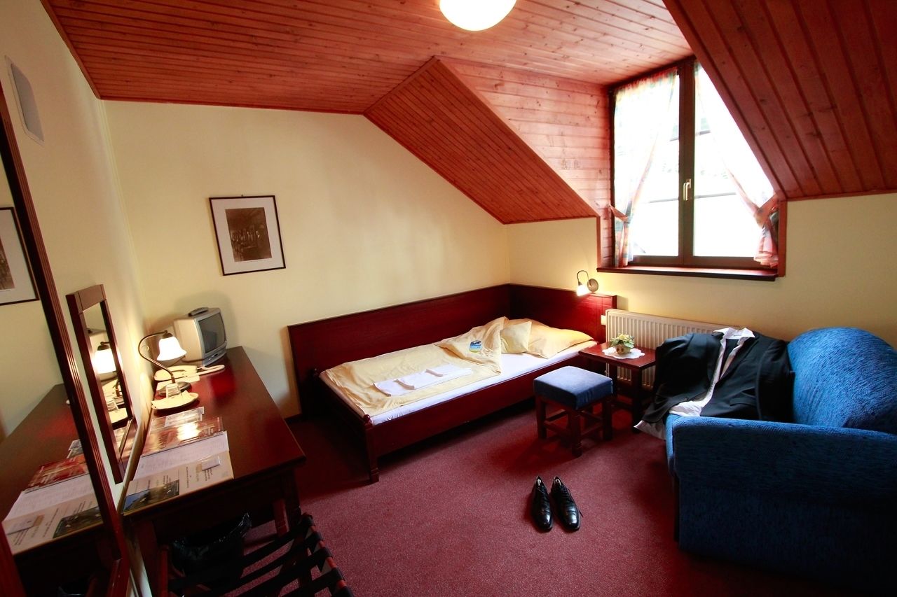 A room with a wooden ceiling, a bed, a desk with a lamp, a chair, and a window.