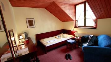 A room with a wooden ceiling, a bed, a desk with a lamp, a chair, and a window.