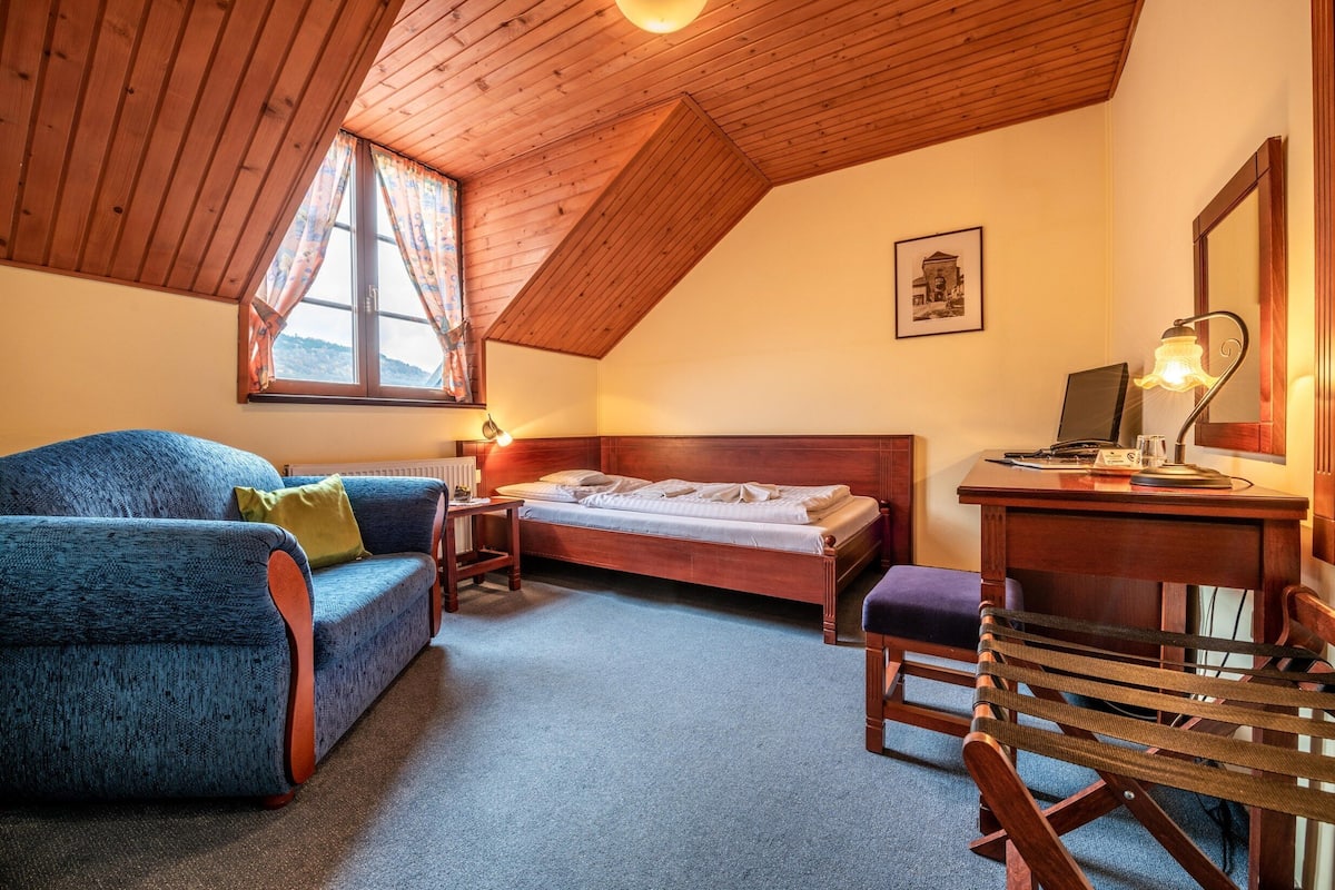 A bedroom with a wooden ceiling, a bed, a blue sofa, a desk, and a chair.