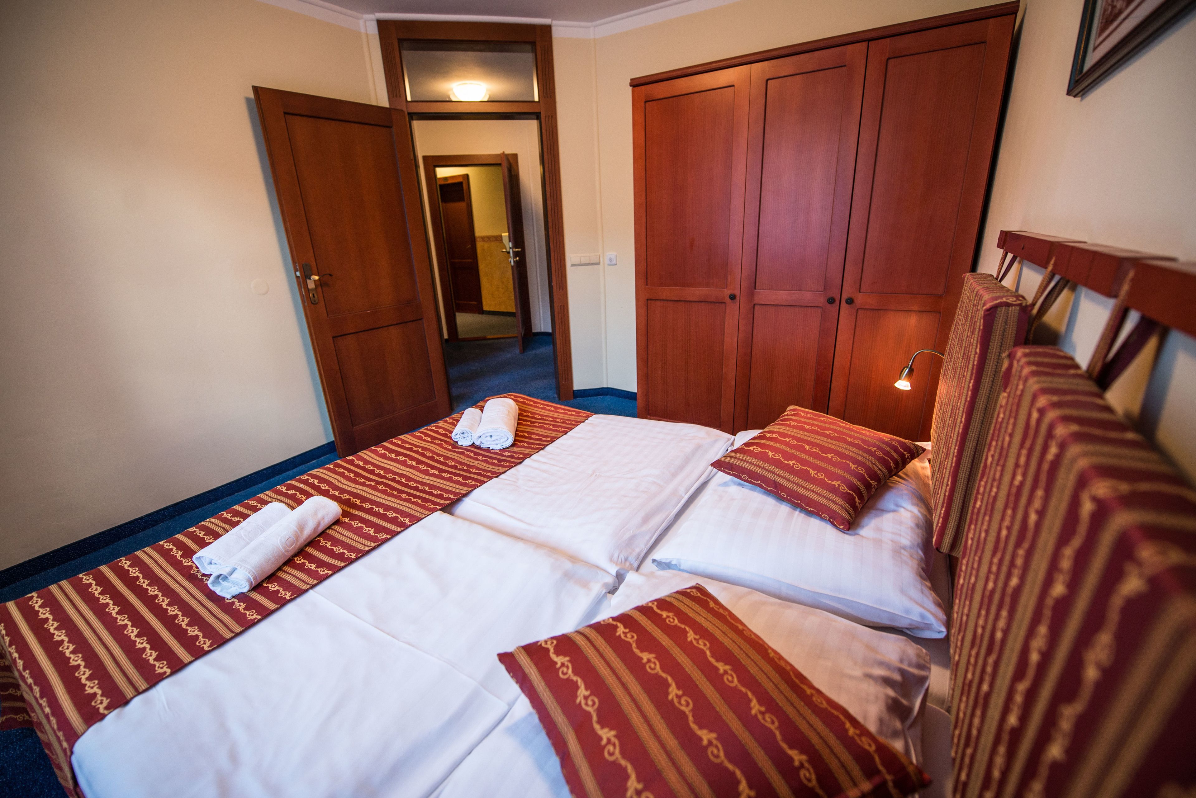 A hotel room with a large bed, two wooden wardrobes, and a hallway leading to another room.