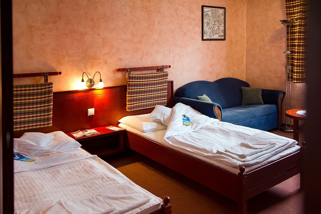 Una camera d'albergo con due letti singoli, un divano, un comodino, una lampada e un quadro appeso al muro.