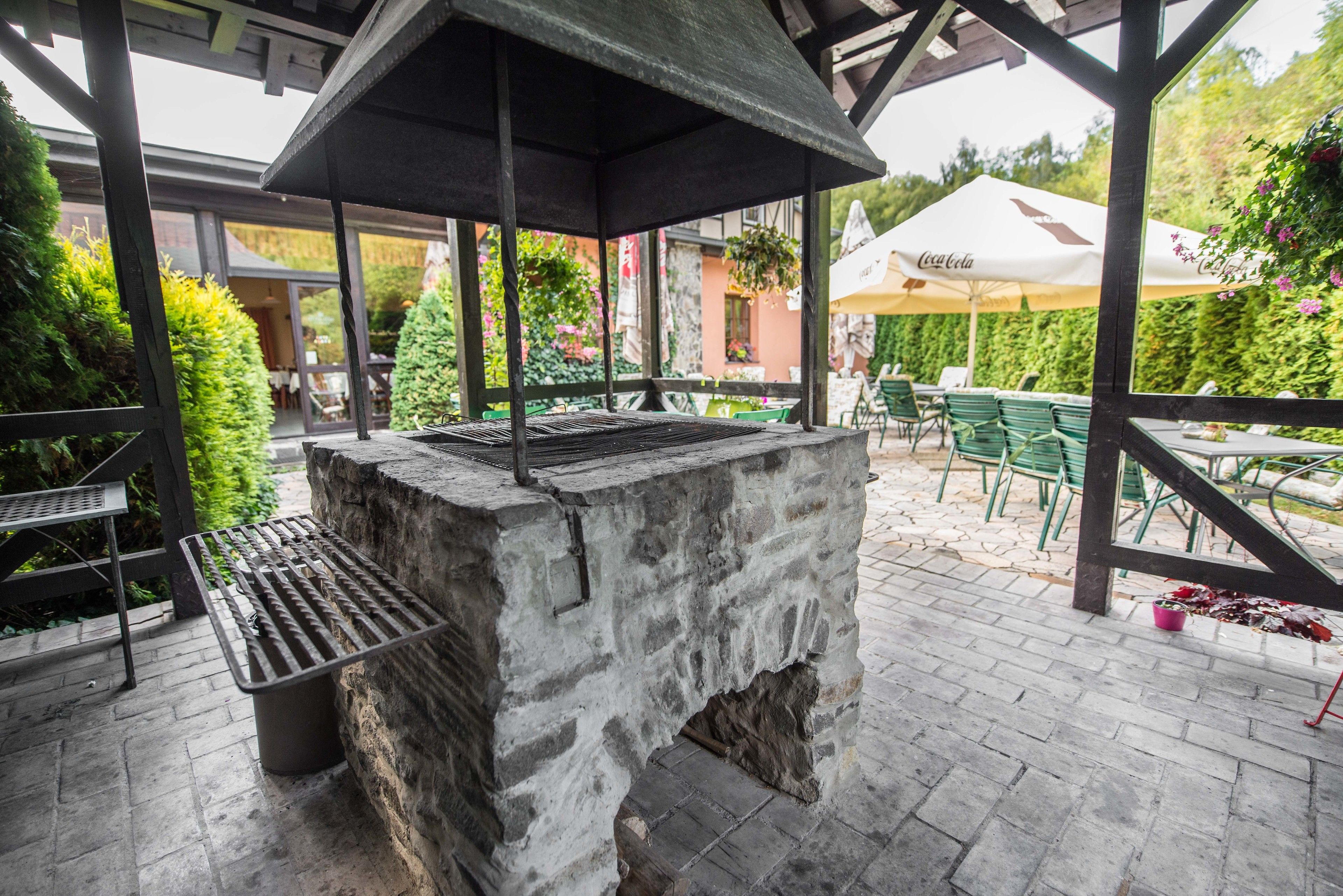 Terrassa exterior amb una barbacoa de pedra, cadires verdes i ombrelles.