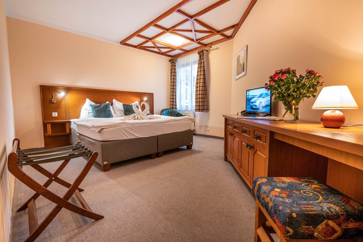 A hotel room with a bed, a desk with a computer, a lamp, a chair, and a window with curtains.