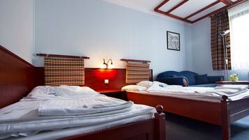 A hotel room with two wooden beds, a nightstand with a lamp, a blue sofa, and a window with curtains.