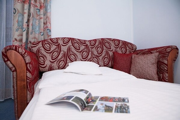 A single bed with a patterned headboard and pillows, a white bedspread, and a magazine on the bed.