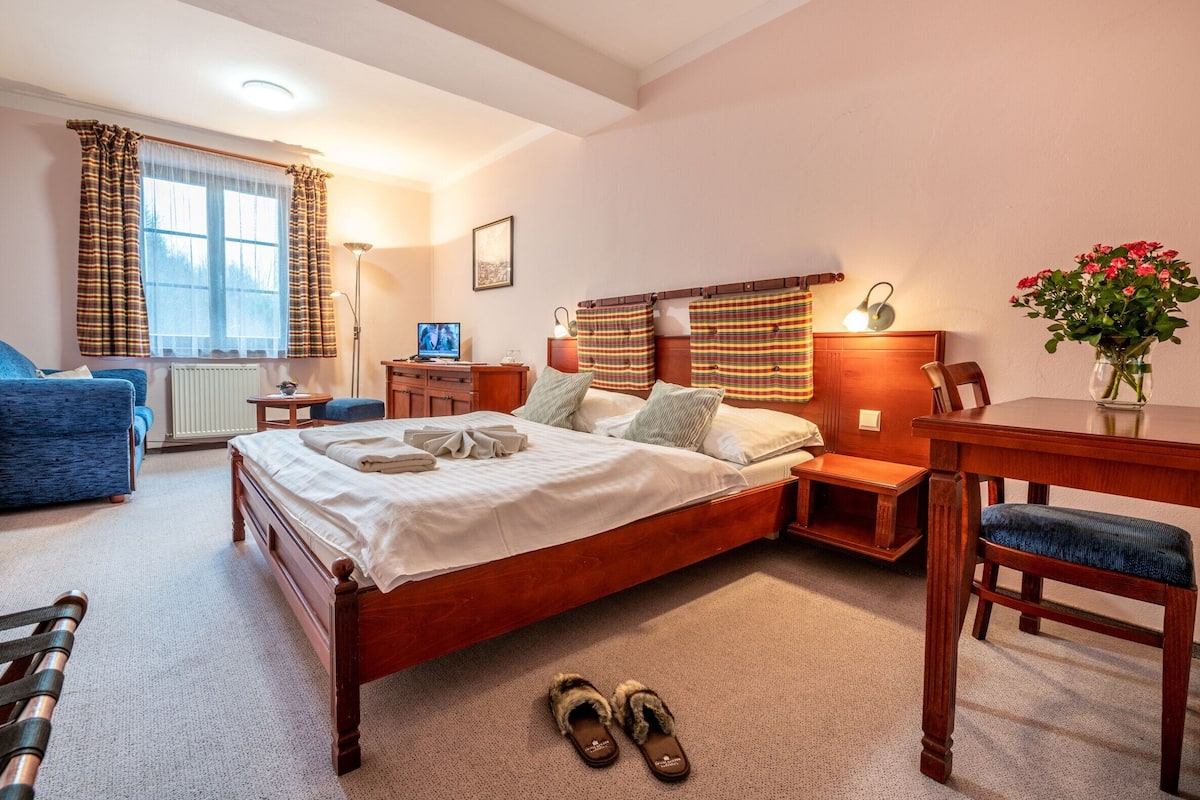 A bedroom with a wooden bed, a desk, a chair, a blue sofa, and a window with curtains.