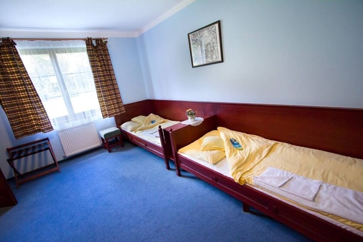 A room with two single beds, a radiator, a window with curtains, and a framed picture on the wall.