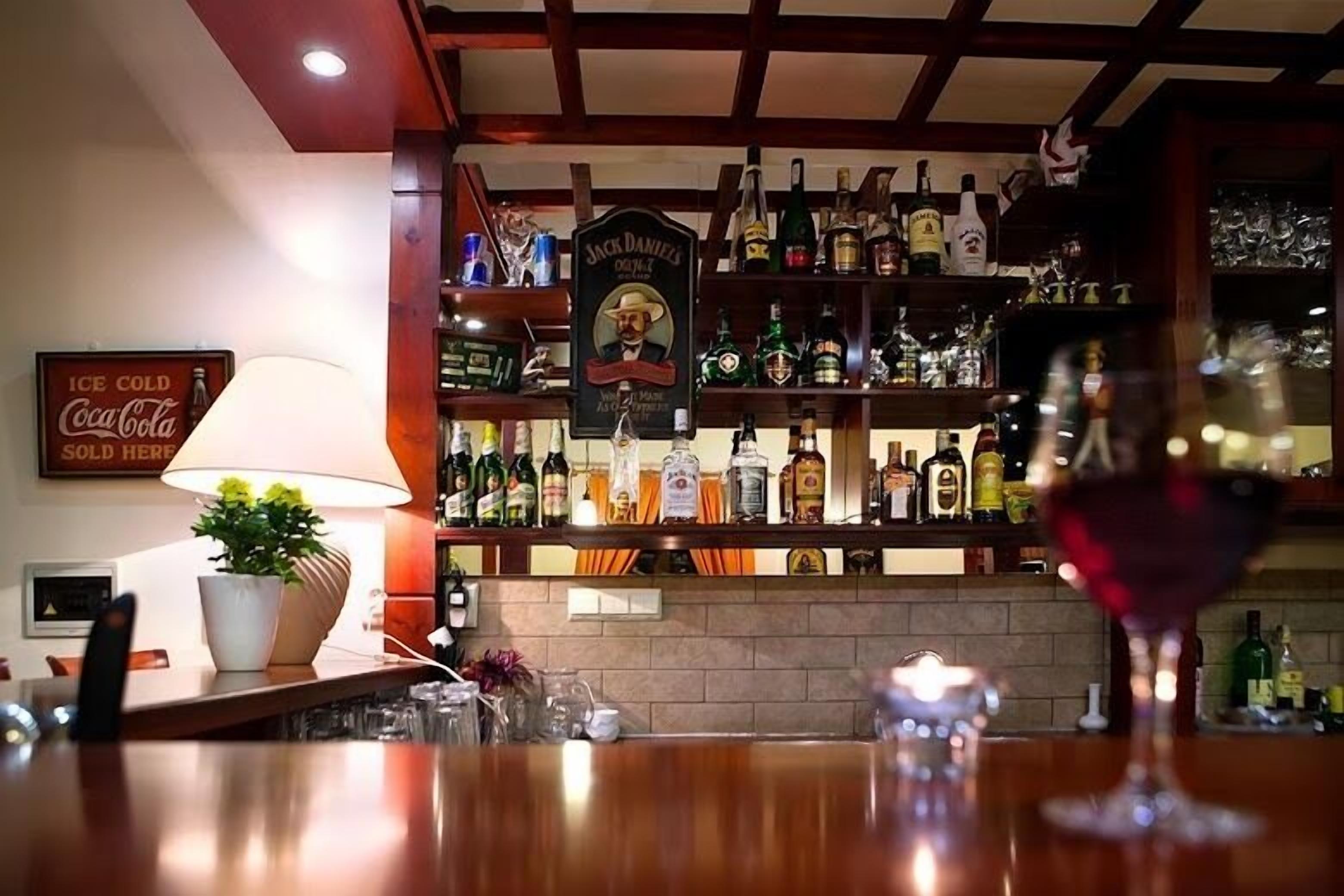 A bar area with shelves of liquor bottles, a glass of red wine, and a Coca-Cola sign.
