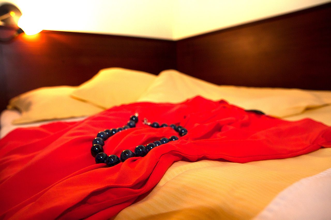 Un letto con un copriletto rosso e una collana nera con perline.
