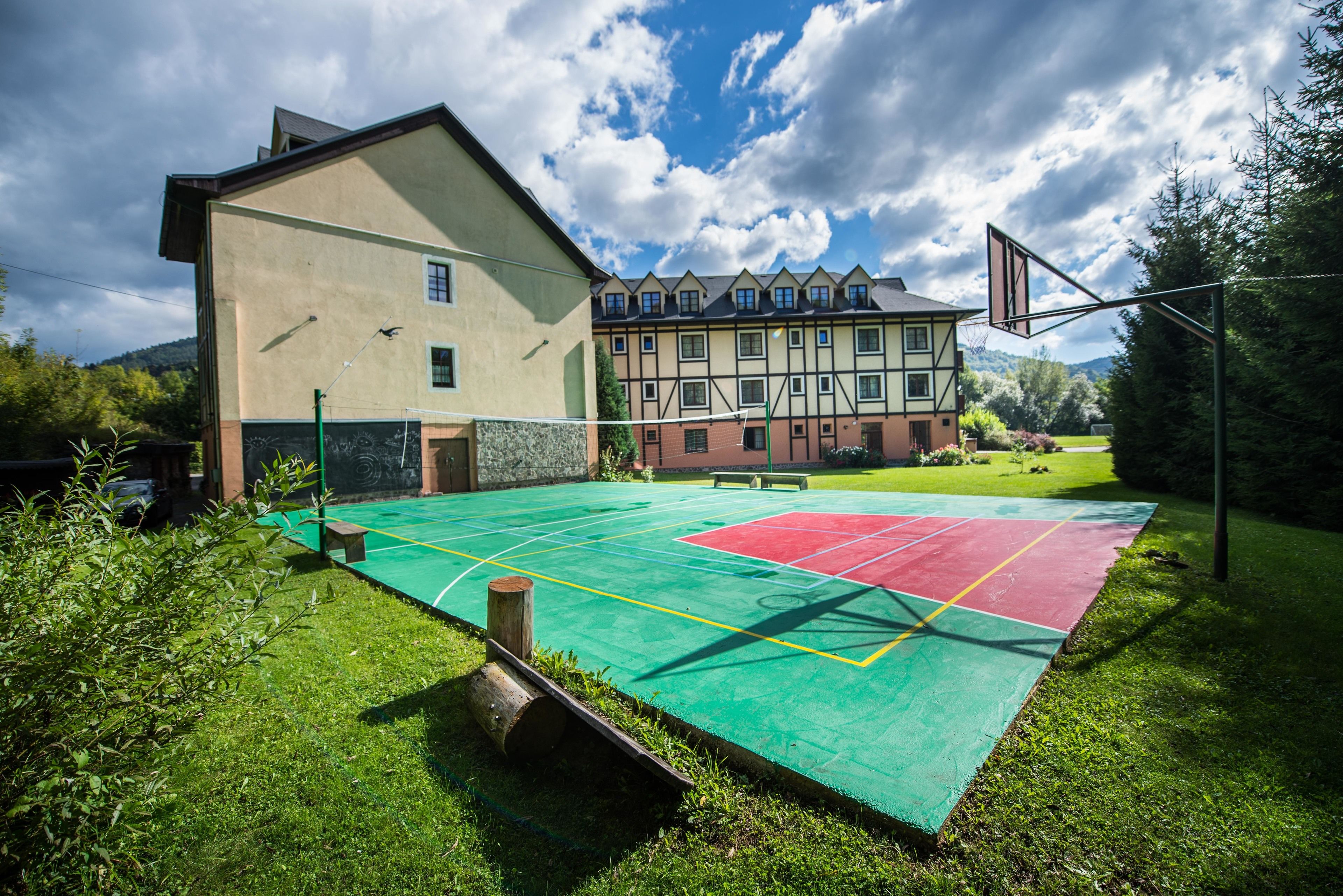 An outdoor basketball court with a green and red playing surface, surrounded by grass and trees.