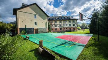 An outdoor basketball court with a green and red playing surface, surrounded by grass and trees.