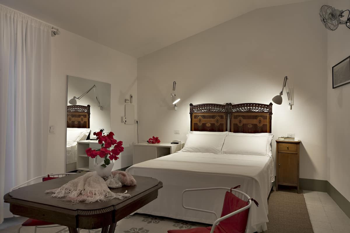 Een hotelkamer met een bed, nachtkastjes, een bureau met een stoel, een spiegel en een rode stoel.