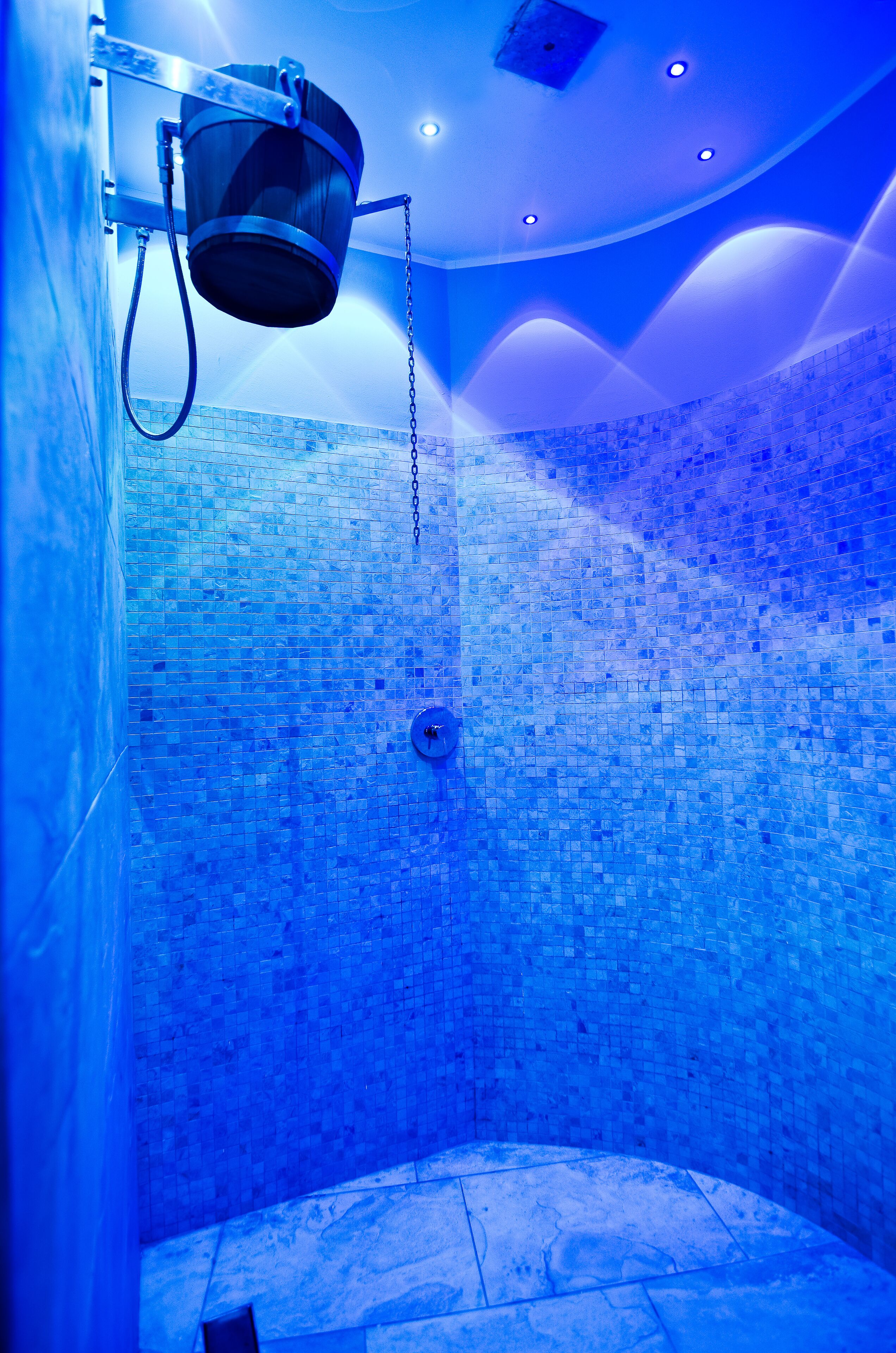 A bathroom with a mosaic tile wall, a shower area, and a ceiling light fixture.