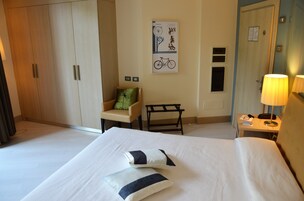 A hotel room with a large bed, a chair, a desk with a lamp, and a wardrobe.