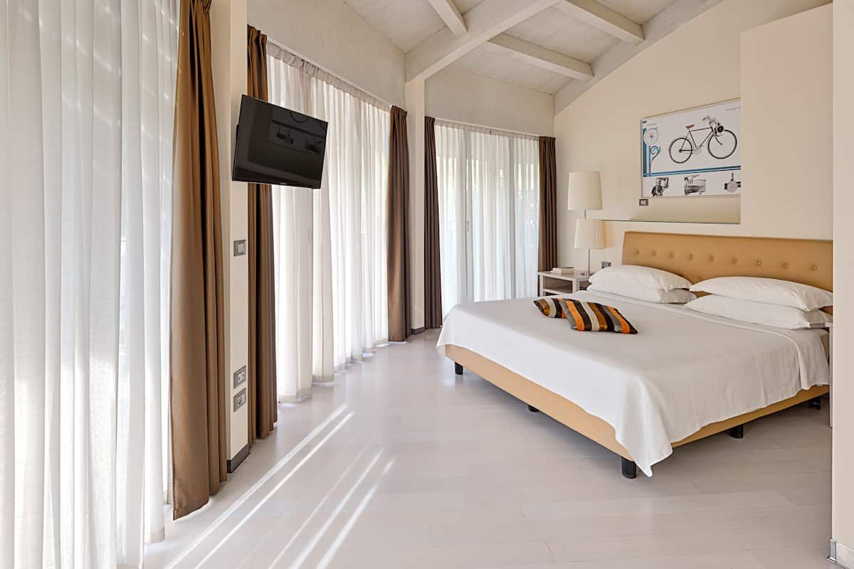 A hotel room with a large bed, a television mounted on the wall, and a bicycle-themed artwork above the bed.