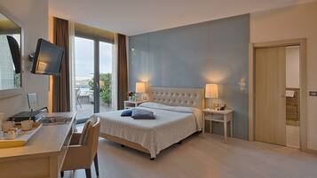 Ein modernes Hotelzimmer mit einem großen Bett, einem Schreibtisch mit Computer und einem an der Wand befestigten Fernseher.