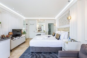 Une chambre d’hôtel moderne, dotée d’un grand lit, d’un bureau, d’une télévision et d’une salle de bain visible à travers une porte ouverte.