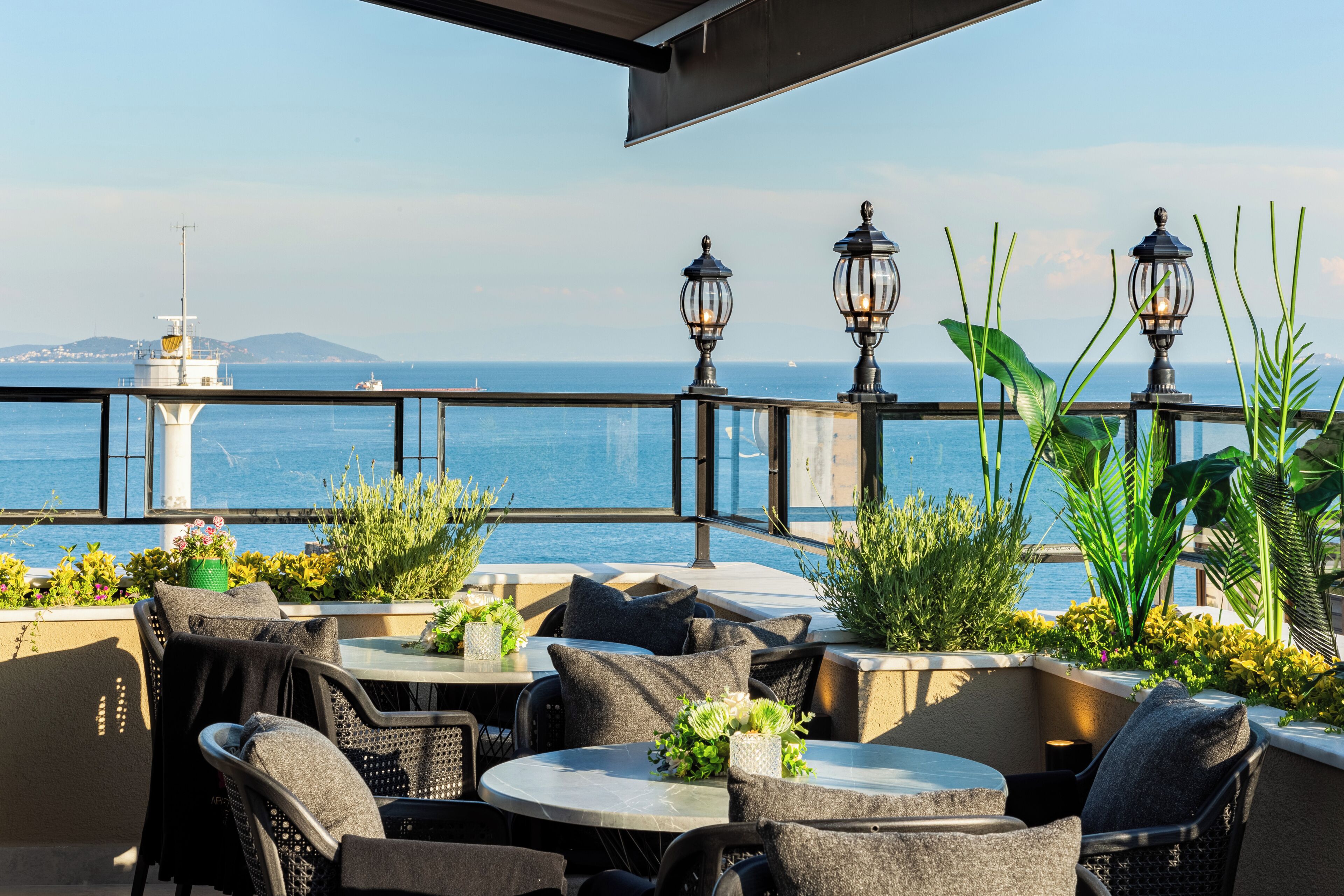 An outdoor seating area with tables and chairs, overlooking a body of water with a distant island and lighthouse.