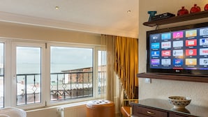 Une chambre d’hôtel avec une grande fenêtre, une télévision, un petit tabouret et un vase décoratif posé sur une commode.
