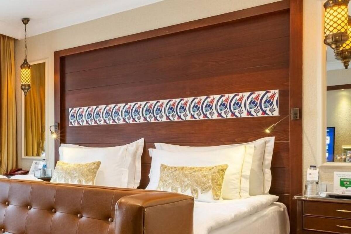 A hotel room with a large bed, a brown leather sofa, a wooden headboard, and a decorative wall panel.