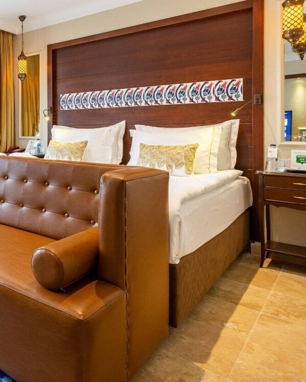 A hotel room with a large bed, a brown leather sofa, a wooden headboard, and a decorative wall panel. - Sadaret Hotel & Suites Istanbul (Istanbul)