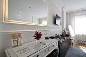 A hotel room with a glass desk, a flat-screen TV mounted on the wall, a large mirror, and a window with sheer curtains. - Sadaret Hotel & Suites Istanbul (Istanbul)