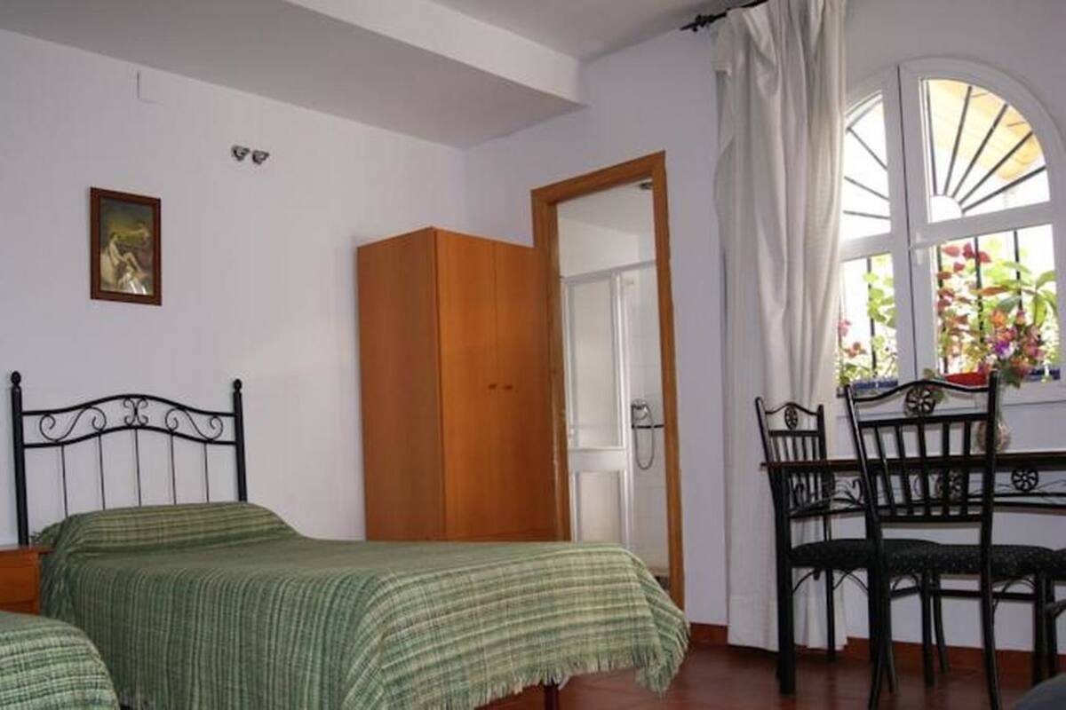 A bedroom with two single beds, a wooden wardrobe, a desk with a chair, and a window with curtains.