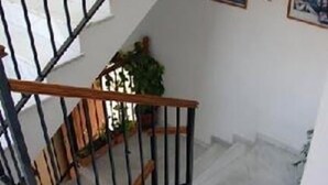 A staircase with a wooden handrail and black balusters, white walls, and a small plant on the landing. - Alcázar (Córdoba)